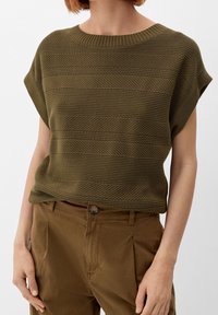 Olive green knitted top with horizontal stripe texture and short sleeves, paired with brown trousers featuring a button closure.