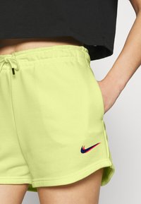 Pantalones cortos Nike de color verde claro con cintura elástica, cierre de cordón y un pequeño logo en rojo y azul marino en el lado izquierdo.