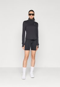Langærmet sort bluse med høj krave, parret med sorte cykelshorts. Reflekterende detaljer og sporty hvide sneakers fuldender outfittet.