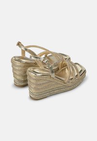 Sandalias de cuña doradas con base de cuerda trenzada. Presentan tiras metálicas, punta cuadrada y adornos de strass decorativos en las tiras.