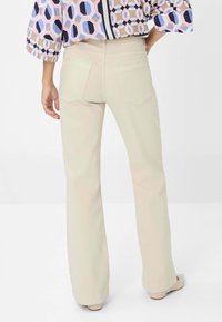 Lichtbeige uitlopende jeans met achterzakken, met een gladde textuur en een op maat gemaakte pasvorm. Zichtbare stiksels in een contrasterende kleur.