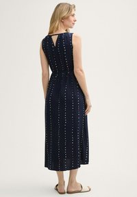 Marineblaues ärmelloses Maxikleid mit weißen vertikalen Punkten, geraffter Taille und Schlüsselloch-Detail im Rücken. Hergestellt aus einem glatten, leichten Stoff.