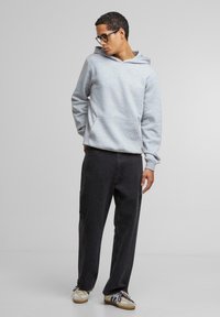 Grå hettegenser med frontlomme, iført med mørke bukser og sneakers. Hettegenseren har en avslappet passform og en kengurulomme for ekstra komfort.