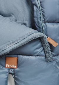 Blå puffy jakke indvendig med blødt, tekstureret for. Har en lynlås og et brunt lædermærke mærket "Elodie." Glat yderstof.