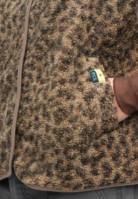 Ζακέτα από φλις σε καφέ και ταμπά χρώματα με υφή ζωοπυθόμενου μοτίβου. Διαθέτει κλείσιμο με κουμπιά και ετι�κέτα PCS στο πλάι κοντά στην τσέπη.