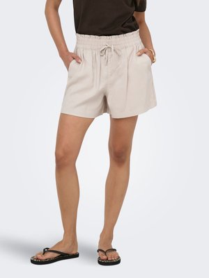 Mujer que lleva pantalones cortos beige con cinturilla elástica y cordón, camiseta negra y chanclas negras con suelas estampadas de leopardo.