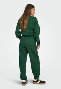 Grøn, oversized sweatshirt og matchende joggers i blødt stof. Joggersne har en elastisk talje og manchetter, kombineret med sorte sneakers.