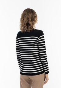 Pulover cu dungi alb-negru, cu mâneci lungi, textură tricotată, guler rotund și secțiune superioară complet neagră. Purtați cu pantaloni bej deschis.