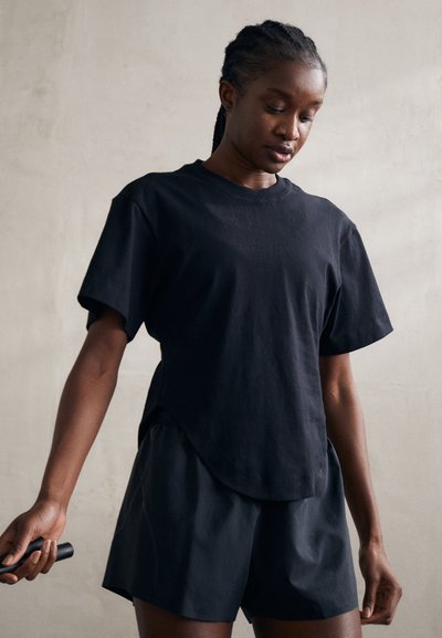 Black cotton t-shirt with short sleeves and a rounded hem, paired with black shorts. Features a relaxed fit and soft texture.