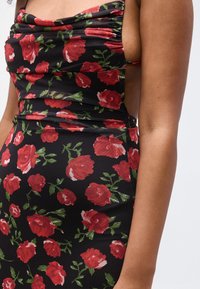 Μαύρο φόρεμα με μοτίβο κόκκινου τριαντάφυλλου στο πάνω μέρος του σώματος και στο μπράτσο, με ντραπέ λαιμόκοψη και αμάνικη σχεδίαση.