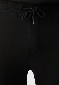 Primer plano de pantalones de punto negros con cintura acanalada y cordón atado en la parte delantera.