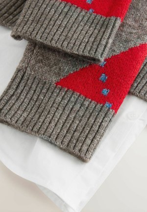 Grauer gestrickter Pullover mit gerippten Bündchen, der rote dreieckige Muster und blaue Punkte aufweist; über einem weißen Hemd mit Kragen drapiert.
