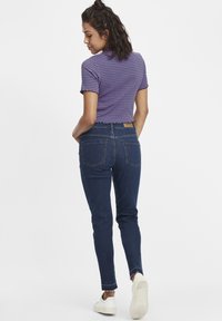 Camisa ajustada de manga corta con rayas moradas y azules; combinada con unos vaqueros de tiro alto de color azul oscuro con bolsillos traseros y dobladillo deshilachado. Zapatos blancos.