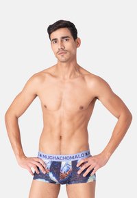 Pánske boxerské šortky s farebným vzorovaným dizajnom a modrou elastickou gumou s nápisom "MUCHACHOMALO". Materiál sa zdá byť mäkký a hladký.