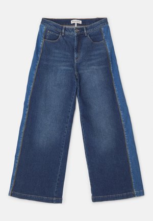 Bredde bukser i middels og lys blå denim med kontrasterende paneler. Har fem lommer, glidelåsgylf og sydd kant.