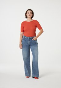 Rode geribbelde top met korte mouwen, hoog-zittende lichtblauwe wijdgerande jeans, met een subtiel logo, gestyled met oranje hoge hakken.