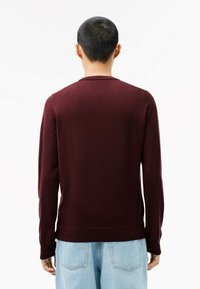 Maglione bordeaux a maniche lunghe con collo girocollo, lavorazione a maglia testurizzata e polsini a coste, abbinato a jeans azzurri chiari.