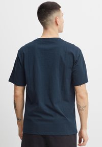Navy blue short-sleeve t-shirt with a relaxed fit. Soft, textured fabric, crew neckline, and minimalistic design. Rear view shows simple styling.