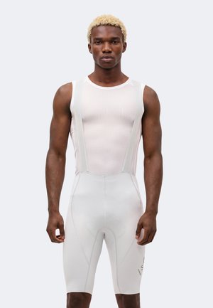 Mies, jolla on lyhyet vaalennetut hiukset, valkoinen hihaton verkkopaita ja valkoiset pyöräilyhousut ilman taustaa.