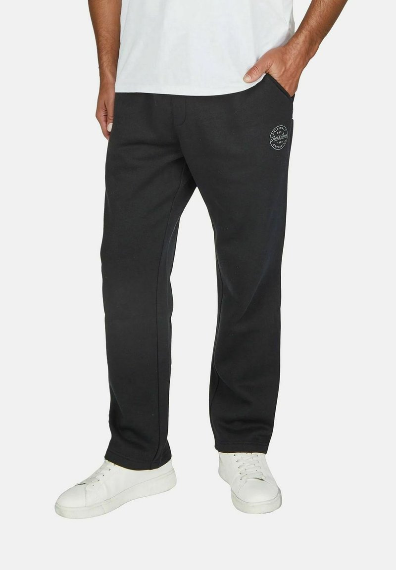 Black sweatpants in soft fabric, featuring a printed logo on the thigh, side pockets, and a relaxed fit. Paired with white sneakers.