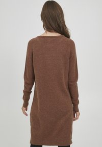 Bruine sweaterjurk gemaakt van een zachte, gestructureerde stof, met lange mouwen, een ronde halslijn en zijsplitten aan de zoom.