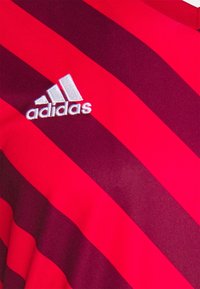 Rød og mørkerød stribet atletisk skjorte med det hvide broderede Adidas-logo på venstre side. Glat, letvægtsstof.