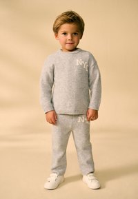 Maglione e pantaloni in maglia grigia con scritta "NYC" in una texture morbida, abbinati a sneakers bianche. Design semplice, schema di colori coerente.