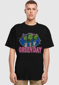 Juodas platūs marškiniai su animacinių zombių grafika, turinčia žalią odą ir spalvingus akcentus, bei dideliu "GREENDAY" tekstu rožine spalva.