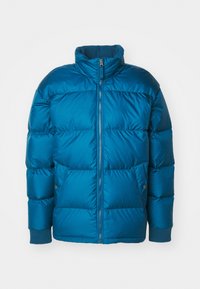 Blågrön puffjacka med hög krage, dragkedja framtill och ribbade muddar. Har stora quiltade sektioner och sidofickor. Mjukt, glänsande material.