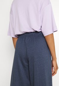 Lös passande lila t-shirt med kort ärm, matchad med mörkblå, elastisk midja, vida byxor. Mjuk tyg med en slät yta.