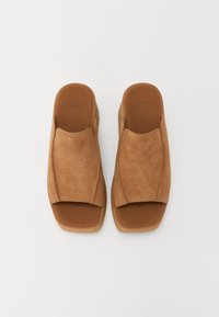 Bruine suède instappers met een platte zool en open tenen, voorzien van een brede bovenste band en een gestructureerde voetbed voor comfort.