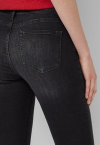 Czarne dżinsy o tapered fit, z jedną kieszenią z tyłu i delikatnym wypłukaniem, pokazane z boku. Gładka tekstura i solidny pas.