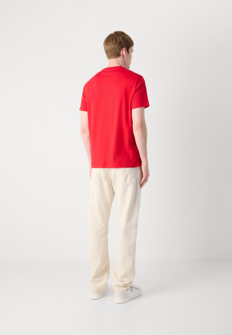 Polo shirt rouge à manches courtes en tissu lisse, associé à un pantalon ample de couleur crème et à des baskets blanches décontractées. Design simple.