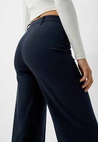 Navy high-waisted trousers made of soft fabric, featuring a tailored fit, subtle side pockets, and a smooth texture.