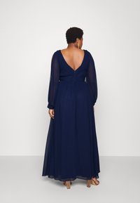 Marineblaues langes Kleid mit fließendem Design und transparenten langen Ärmeln. Es hat einen tiefen V-Ausschnitt auf der Rückseite und eine sanft geraffte Taille für eine schmeichelhafte Passform.