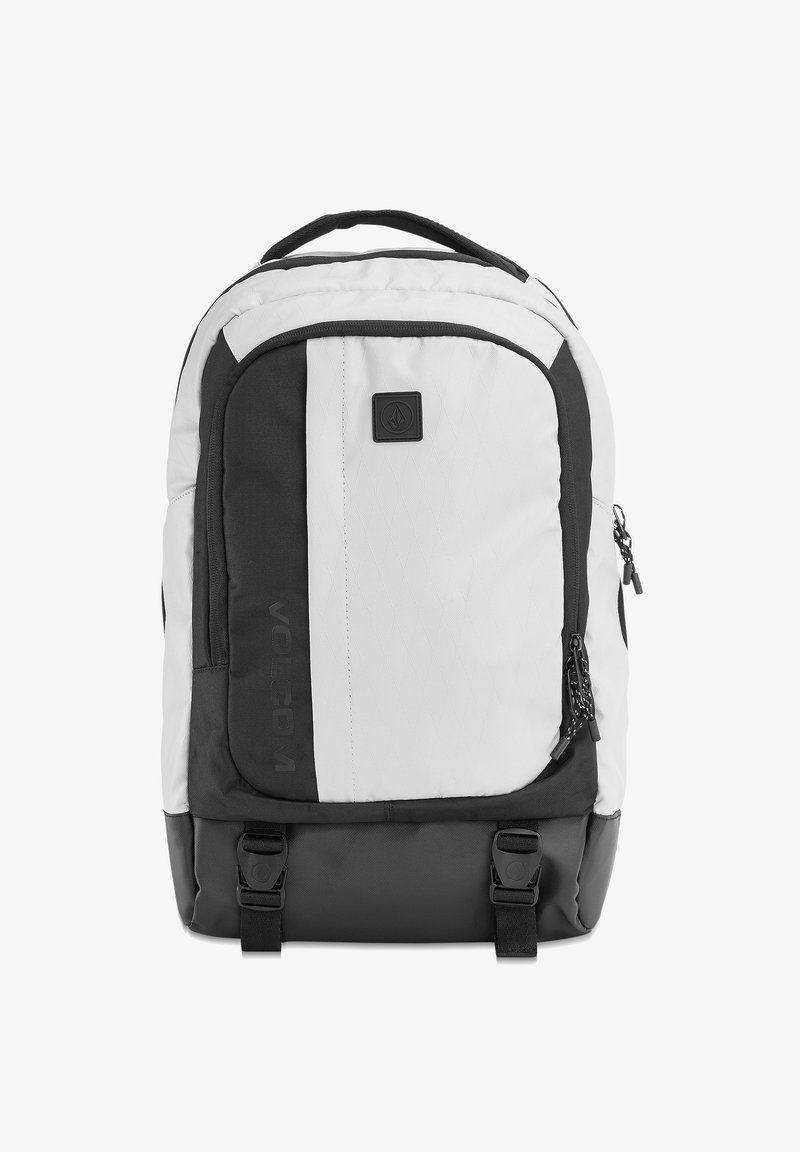 Zaino bianco e nero con spallacci imbottiti, tasche con zip e dettagli con logo. Presenta un tessuto strutturato con un motivo a diamante su un lato.