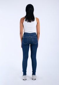 Skinny dark blue jeans with a high waist, complemented by a white ribbed tank top and light-colored sporty shoes.