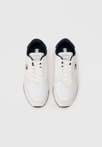 Baltas sneakers ar tumši ziliem akcentiem, kas veidoti no gludas auduma un zamša materiāla, ar apaļu purngalu, plakanu šņorēšanu un logotipu sānos.
