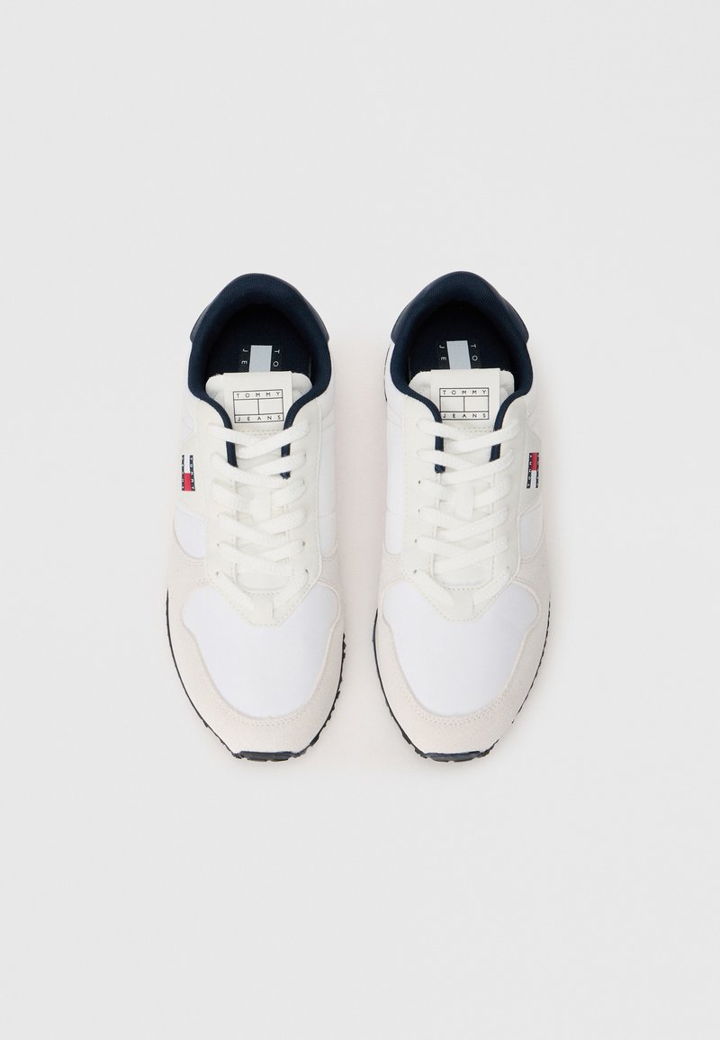 White sneakers with navy accents, featuring a mix of smooth textile and suede materials, round toe, flat laces, and a logo on the side.