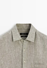 Hellbeiges Leinen-Hemd zum Zumachen mit Kragen und Brusttasche, Etikett zeigt "Massimo Dutti" und "100% Leinen, hergestellt in China."