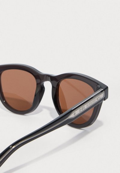 Černé plastové sluneční brýle s hnědými skly, tvar kočičích očí, výrazný rám a kovové detaily na spáncích. Obsahují logo Burberry.