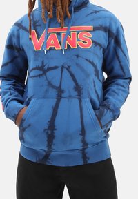 Blauer Batik-Hoodie mit einem großen roten "VANS"-Logo auf der Brust, einer Kängurutasche und Kordelzügen. Weicher Stoff, lockere Passform und lange Ärmel.