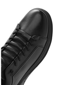 Czarny skórzany tenisówka z wyściełanym językiem, przeszywanymi panelami, czarnymi sznurowadłami i teksturowaną gumową podeszwą.