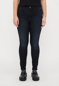 Tmavě modré skinny džíny vyrobené z denimové látky, s předním zapínáním na knoflík, poutky na opasek a tradičním pětipocketovým stylem.
