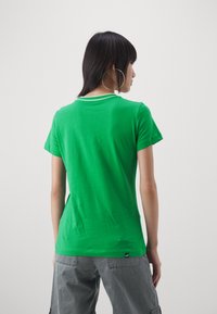 T-shirt verde in cotone con maniche corte, con un colletto a righe bianche e un'etichetta vicino all'orlo. La texture appare liscia e morbida.