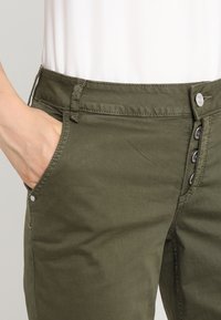 Olijfgroene katoenen blend broek met een gladde textuur, voorzien van zijzakken en een knoopsluiting met metalen hardware.