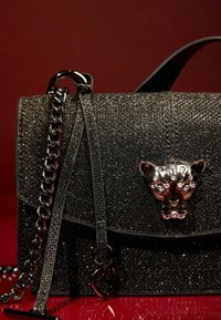 Borsa nera scintillante con tracolla a catena, caratterizzata da una chiusura a forma di pantera in argento lucido e dettagli di superficie testurizzati.