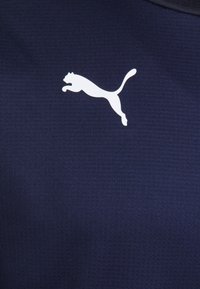 Logo di un puma bianco in salto stampato su un tessuto texturizzato blu scuro, centrato nella parte superiore del petto.