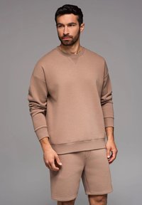 Beige Sweatshirt- und Shorts-Set aus weichem Stoff. Das Sweatshirt hat einen Rundhalsausschnitt und gerippte Bündchen, während die Shorts einen elastischen Bund haben.