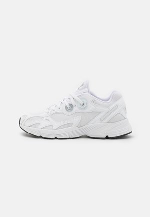 Białe sportowe buty typu sneaker z panelami z siateczki, sznurowanym zapięciem i teksturowaną podeszwą, pokazane z profilu prawej strony na jasnym tle.